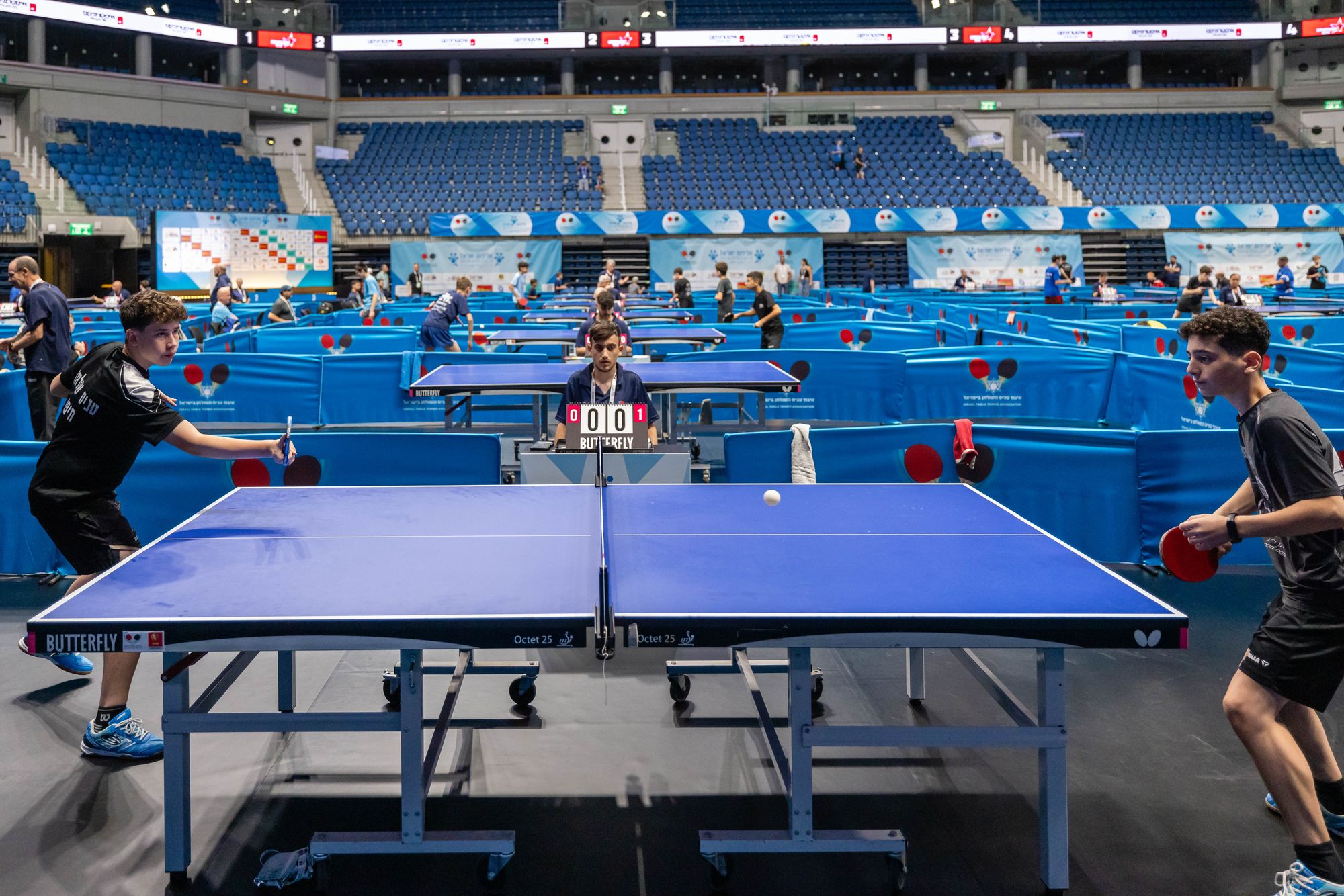 Des joueurs s'affrontent lors d'un tournoi de tennis de table animé, dans une vaste salle omnisports.